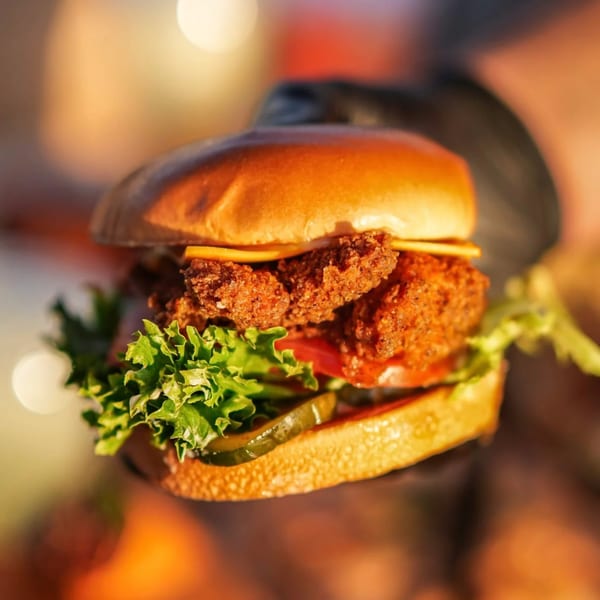 Close-up of a Hot Chicks Food Truck fried chicken sandwich with cheese, lettuce, tomato, and pickles.