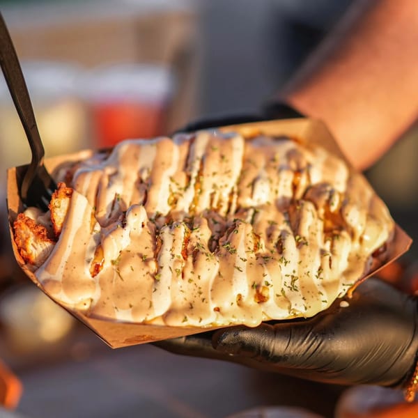 Hands in black gloves holding a tray of Hot Chicks Food Truck's loaded fries with sauce and herbs.