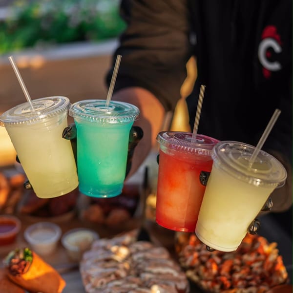 Four colorful frozen drinks, including yellow, blue, and red, held by a person in a black shirt.