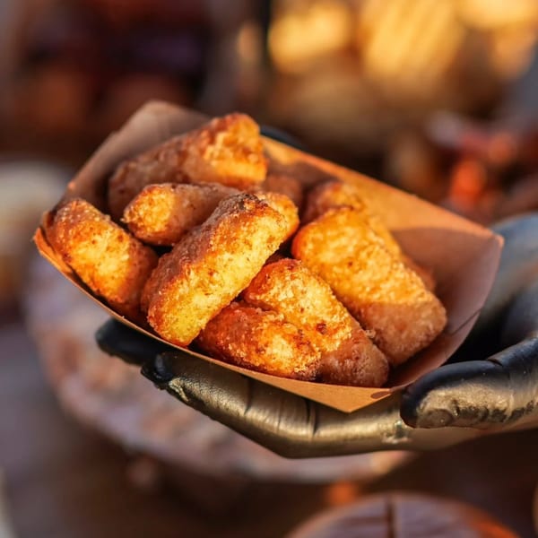 A hand in a black glove holds a paper tray filled with golden-brown fried cheese curds.
